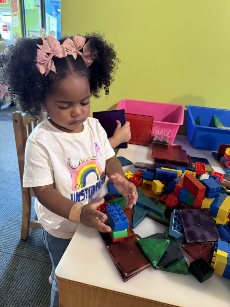 A child is standing at a desk playing with multi-colored blocks.
